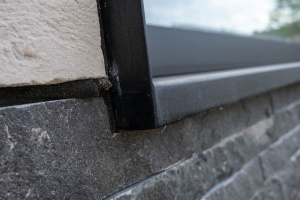 Zwarte aluminium vensterbank met kopschot op een gevel in natuursteen